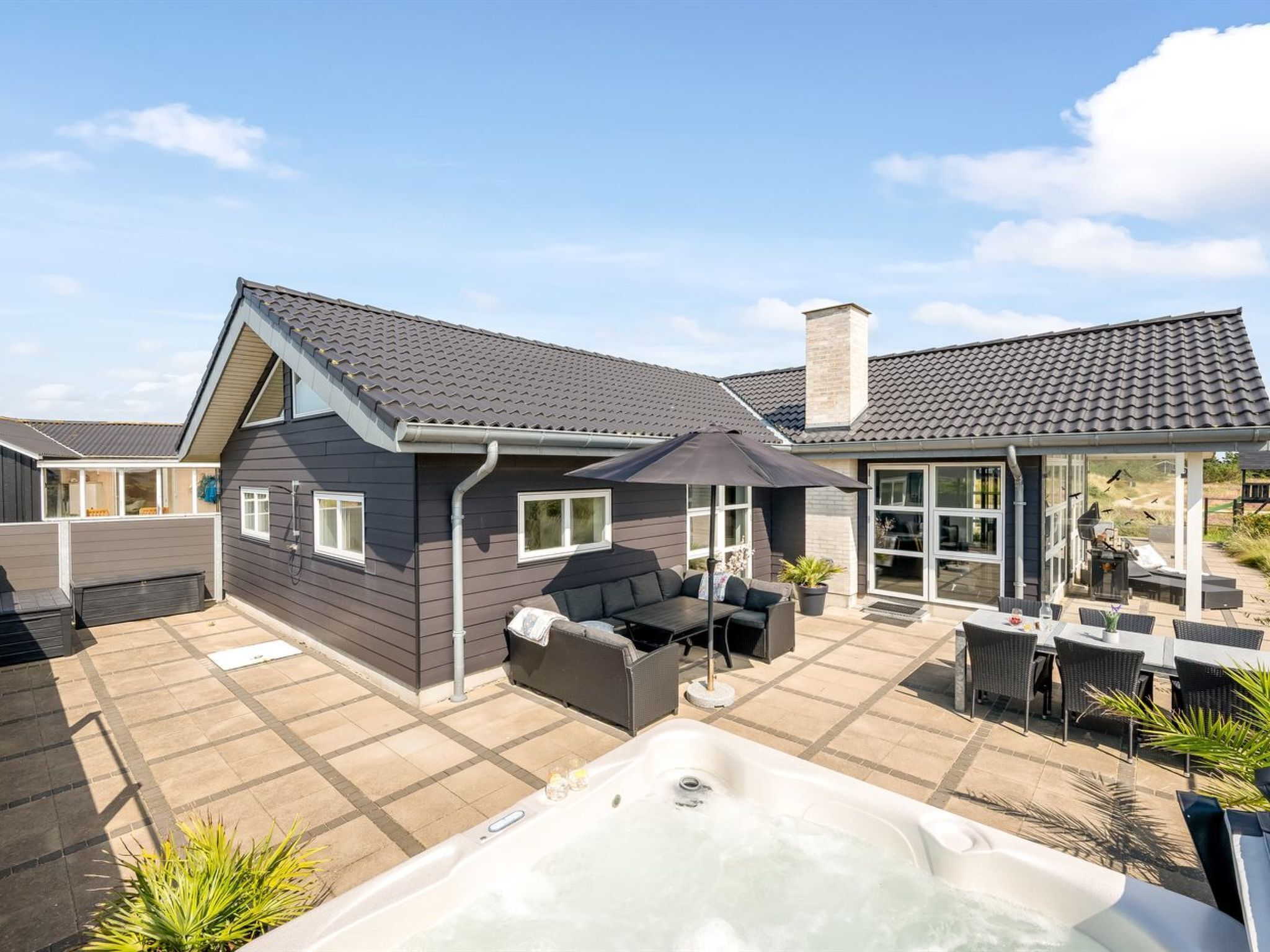 Ein modernes Haus mit Terrasse, ausgestattet mit Whirlpool, Sitzgelegenheiten im Freien und einem überdachten Essbereich.