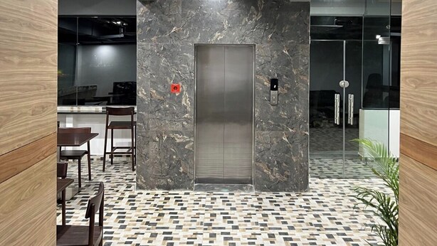 An elevator in a modern office space with a patterned floor and wooden ceiling beams. - Palladium Luxury Suites  (Hyderabad)
