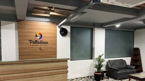 A reception area with a wooden reception desk, a clock, a potted plant, a sofa, and a bookshelf. - Palladium Luxury Suites  (Hyderabad)