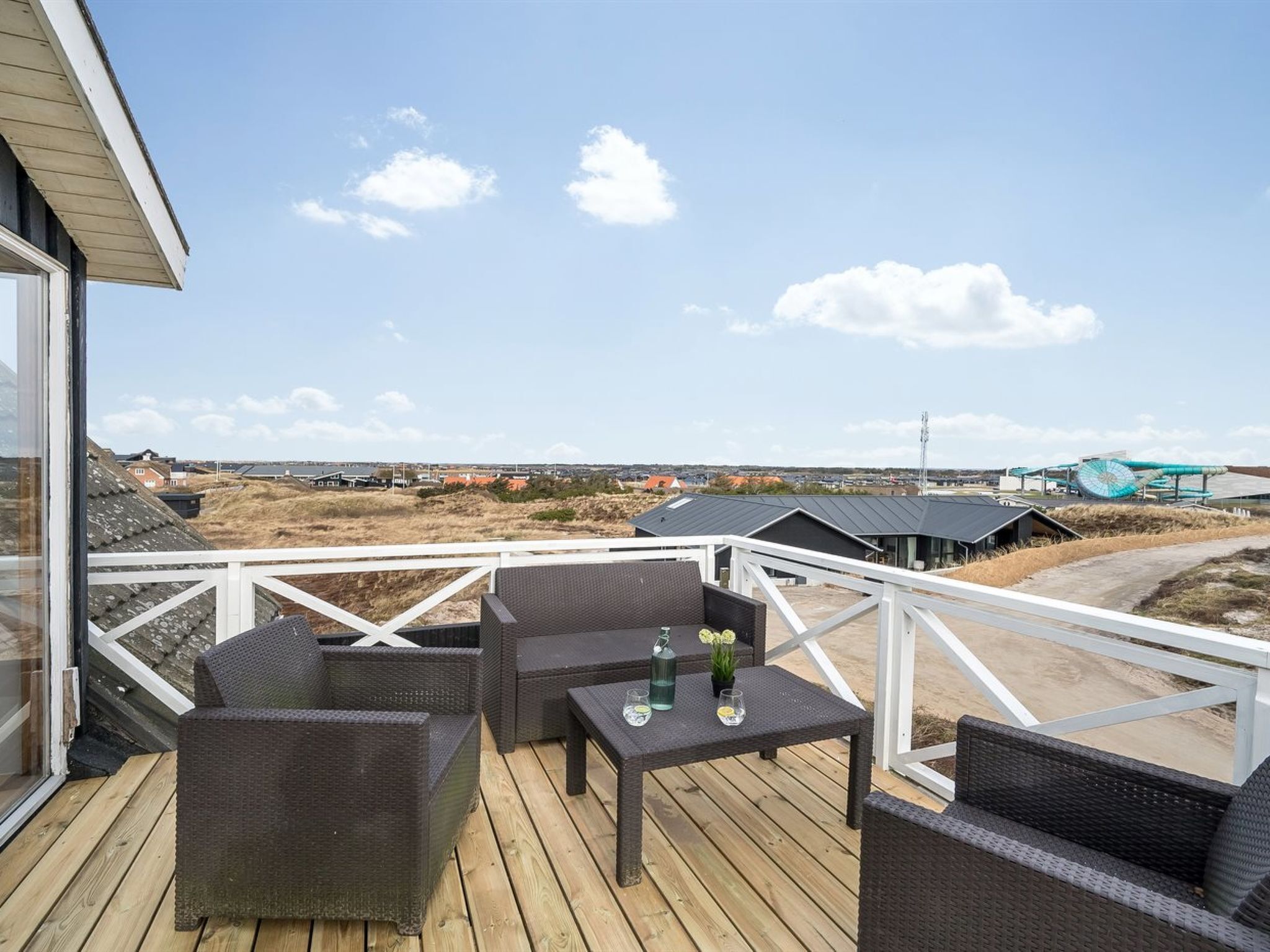 Een terras met rieten meubels en een tafel, met uitzicht op een landschap met gebouwen en een waterzuiveringsinstallatie.