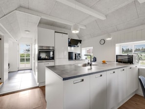 A modern kitchen with white cabinetry, a central island, a built-in oven, and a microwave.
