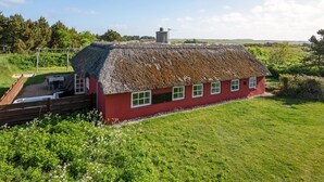Una casa roja con techo de paja, un porche de madera y un patio cubierto de césped.