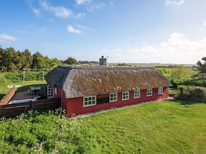 Ein rotes Haus mit einem Strohdach, einer Holzterrasse und Blick auf die Landschaft.