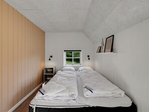 Ein Schlafzimmer mit zwei Betten, einem Fenster, einem Regal mit gerahmten Bildern und einem Nachttisch.
