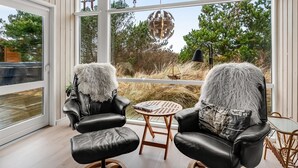 Une pièce moderne avec deux fauteuils en cuir, une petite table ronde et une grande fenêtre donnant sur l’extérieur.