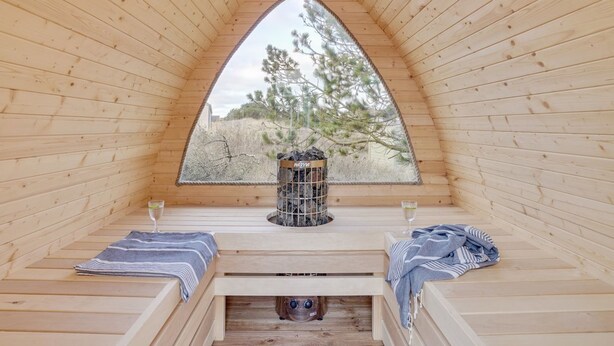 Une cabane en bois chaleureuse, dotée d’une fenêtre triangulaire, d’une petite table avec une bougie et d’un banc recouvert d’une couverture.
