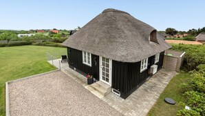 Ett svart hus med ett halmtak, en grusuppfart och en liten trädgård.