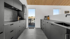 Una cuina moderna amb armaris grisos, un sostre de fusta i vista cap a l'exterior.