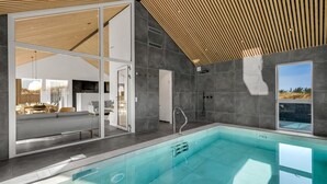 Una piscina coberta moderna amb un envàs de vidre, parets de rajola grisa i un sostre de fusta.