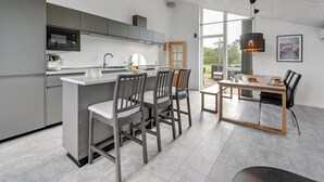 Eine moderne Küche mit einer zentralen Kochinsel, grauen Schränken und einem Essbereich mit einem Holztisch und Stühlen.