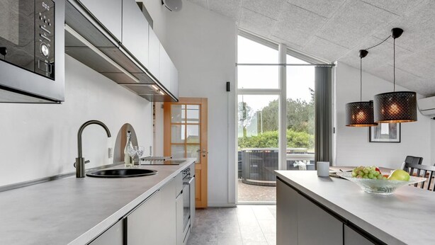Eine moderne Küche mit einer großen Kochinsel, Edelstahlgeräten und Blick auf eine Terrasse.