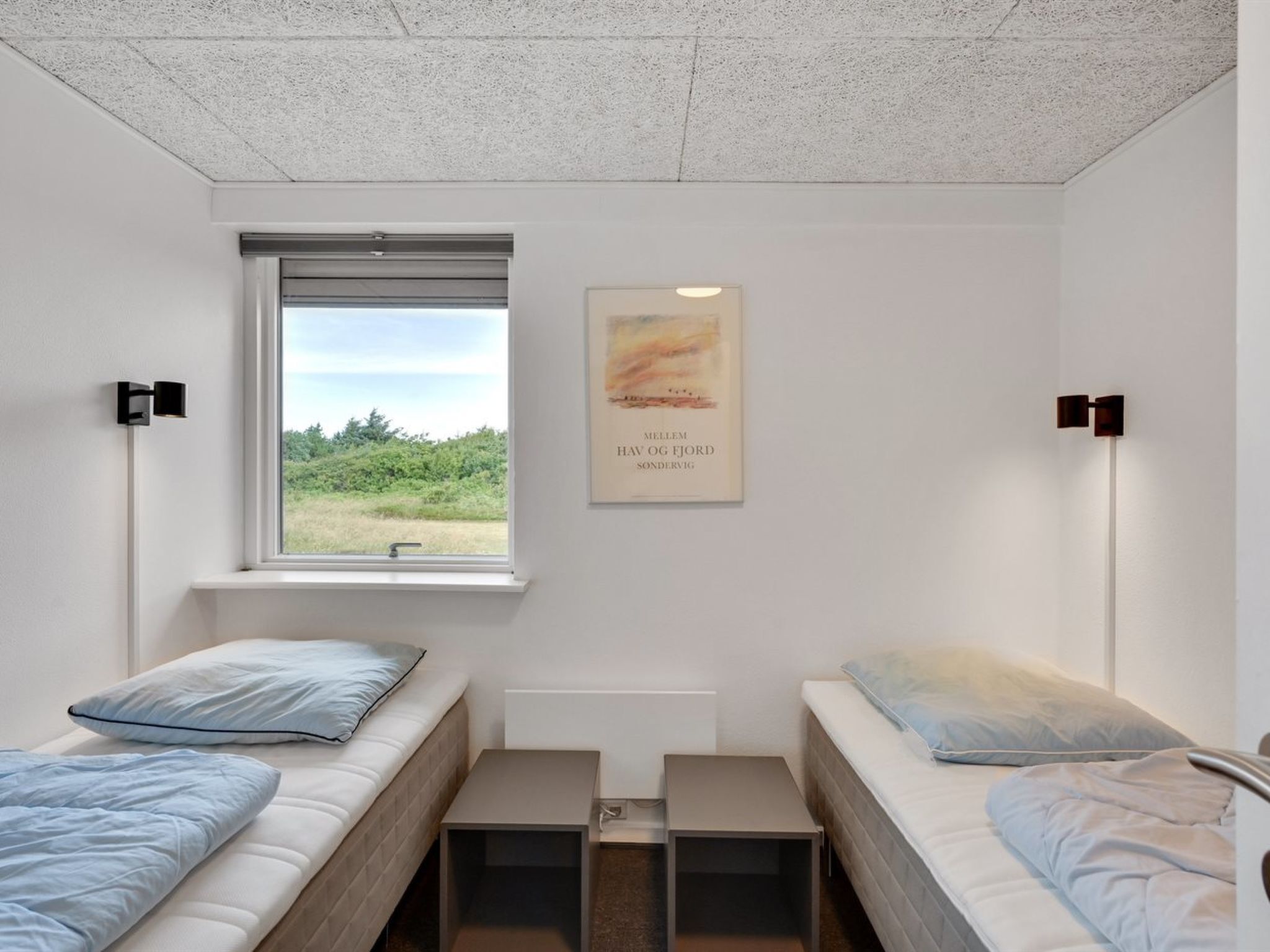 Une chambre avec deux lits, une fenêtre, un radiateur et un tableau encadré au mur.