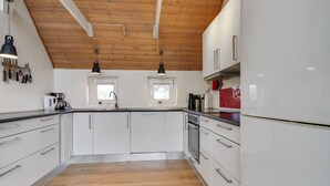 A modern kitchen with white cabinets, a wooden ceiling, and two windows.