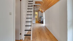 A narrow hallway with wooden flooring and white walls, leading to a staircase with black steps and white railings.