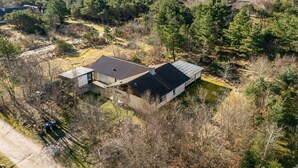 Une maison moderne dotée d’un toit recouvert de panneaux solaires, entourée d’une forêt dense.