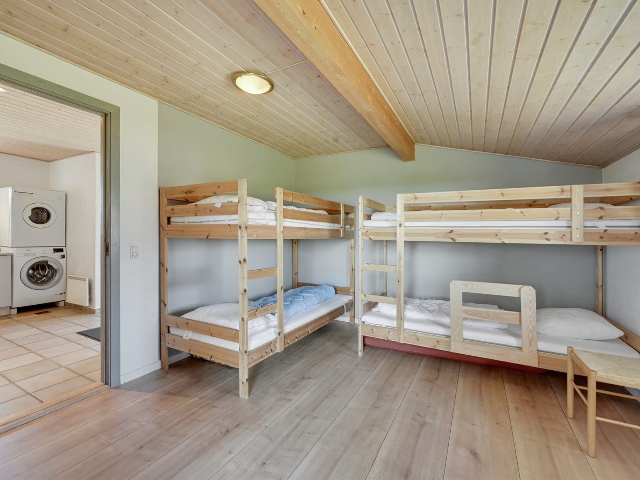 A dormitory room with bunk beds, a washing machine, and a wooden ceiling.