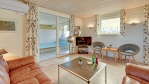 Un salon moderne avec un plafond en bois, une porte vitrée donnant sur une piscine, un téléviseur et deux fauteuils.
