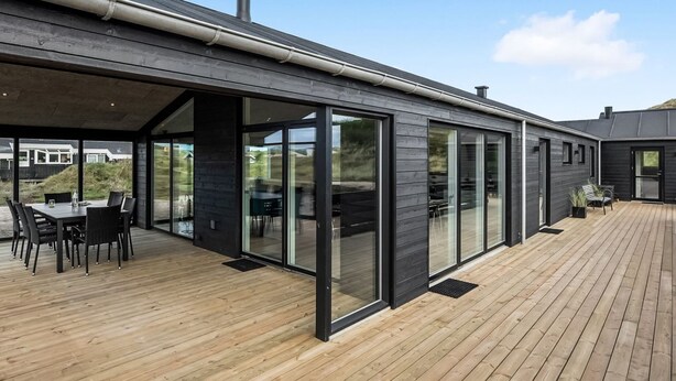 Uma casa moderna com um terraço amplo, portas de correr de vidro e uma chaminé.