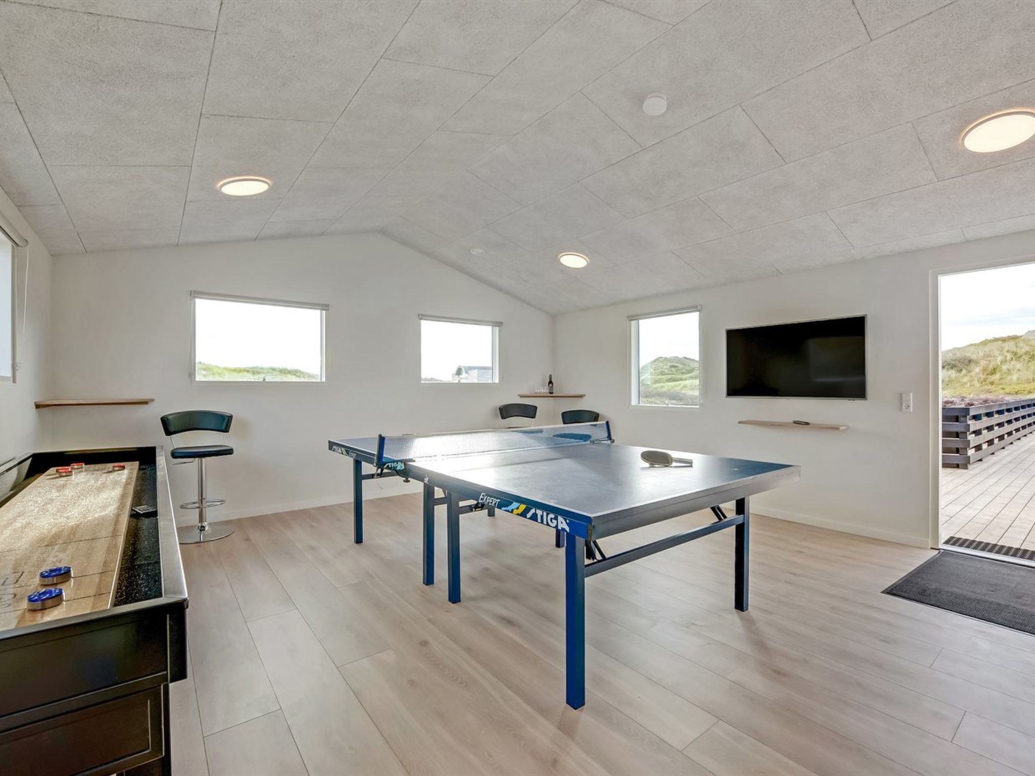 Une pièce spacieuse équipée d’une table de ping-pong, d’un coin bar et d’un téléviseur fixé au mur.