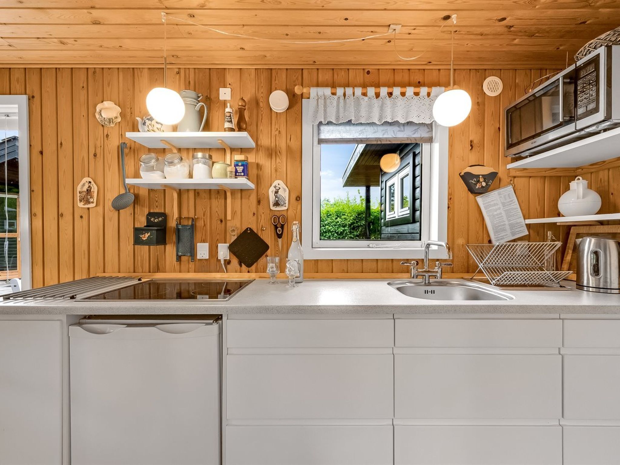Een moderne keuken met houten wanden, witte kasten en een raam met uitzicht op groen.