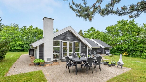 Une maison moderne dotée d’un patio comprenant une table et des chaises, une cheminée et un barbecue.