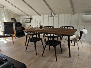 A dining area with a wooden table, black chairs, a hanging light fixture, a fireplace, and a fur-covered chair.