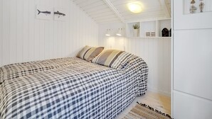 Une chambre à coucher avec une couvre-lit à carreaux, un plafond blanc et une étagère murale ornée d’objets décoratifs.