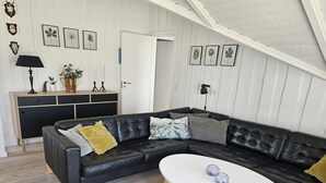 Un salon moderne avec un canapé d’angle en cuir noir, une table basse blanche et un plancher en bois.