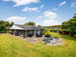 A modern house with a patio, a small garden, and a lawn.