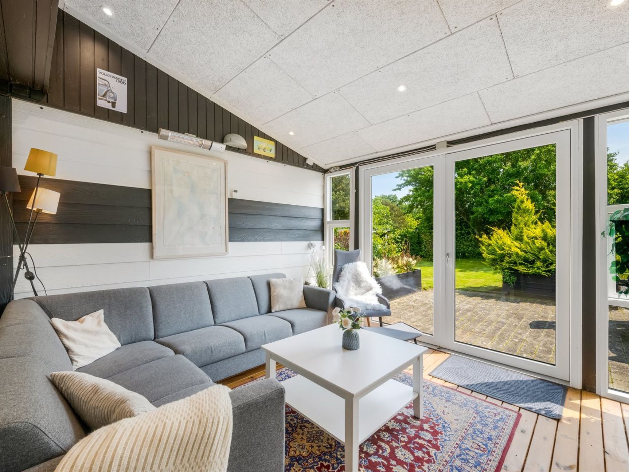 Un salon moderne avec un canapé gris, une table basse blanche et une grande porte-fenêtre coulissante donnant sur un jardin.