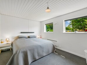 A modern bedroom with a bed, bedside tables, a window with a view of greenery, and a ceiling with a light fixture.