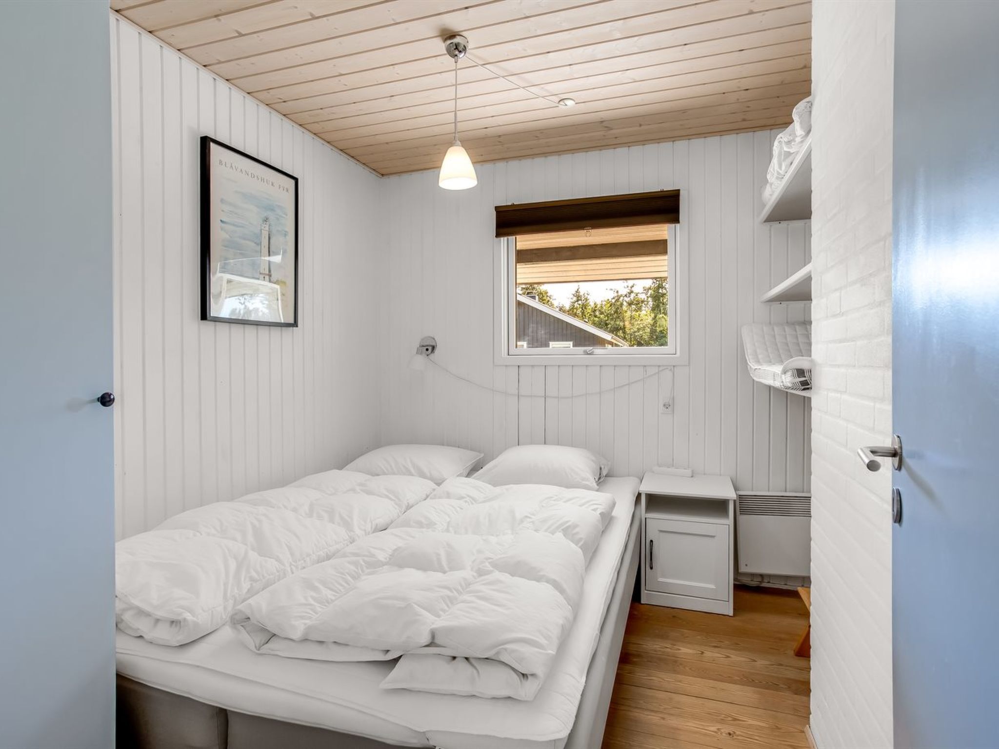 A bedroom with a bed, a window, a bedside table, and a wall-mounted light fixture.