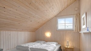 A cozy bedroom with a wooden ceiling, a large window with curtains, a bedside table with a lamp, and a bed with pillows and a blanket. - "Anu" - 300m to the fjord by Interhome (Hemmet)
