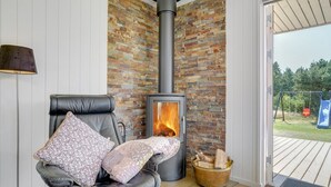 A cozy room with a stone fireplace, a leather chair with floral cushions, and a view of a wooden deck outside. - "Thorvor" - 1.5km from the sea by Interhome (Blåvand)