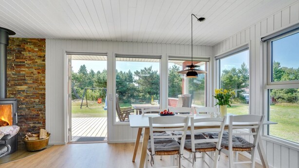 A dining area with a fireplace, white wooden furniture, and large windows offering a view of the outdoors. - "Thorvor" - 1.5km from the sea by Interhome (Blåvand)