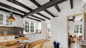 Una cocina amplia con armarios blancos, una mesa de comedor de madera, sillas de mimbre y una lámpara colgante.