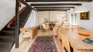 Amplia sala de estar con escalera de madera, chimenea y mesa de comedor con sillas.