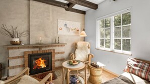 Una sala de estar acogedora con chimenea, un sofá cómodo, una silla de madera y un ventanal grande.