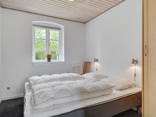 A bedroom with a bed, a window with a view of greenery, and a bedside lamp.