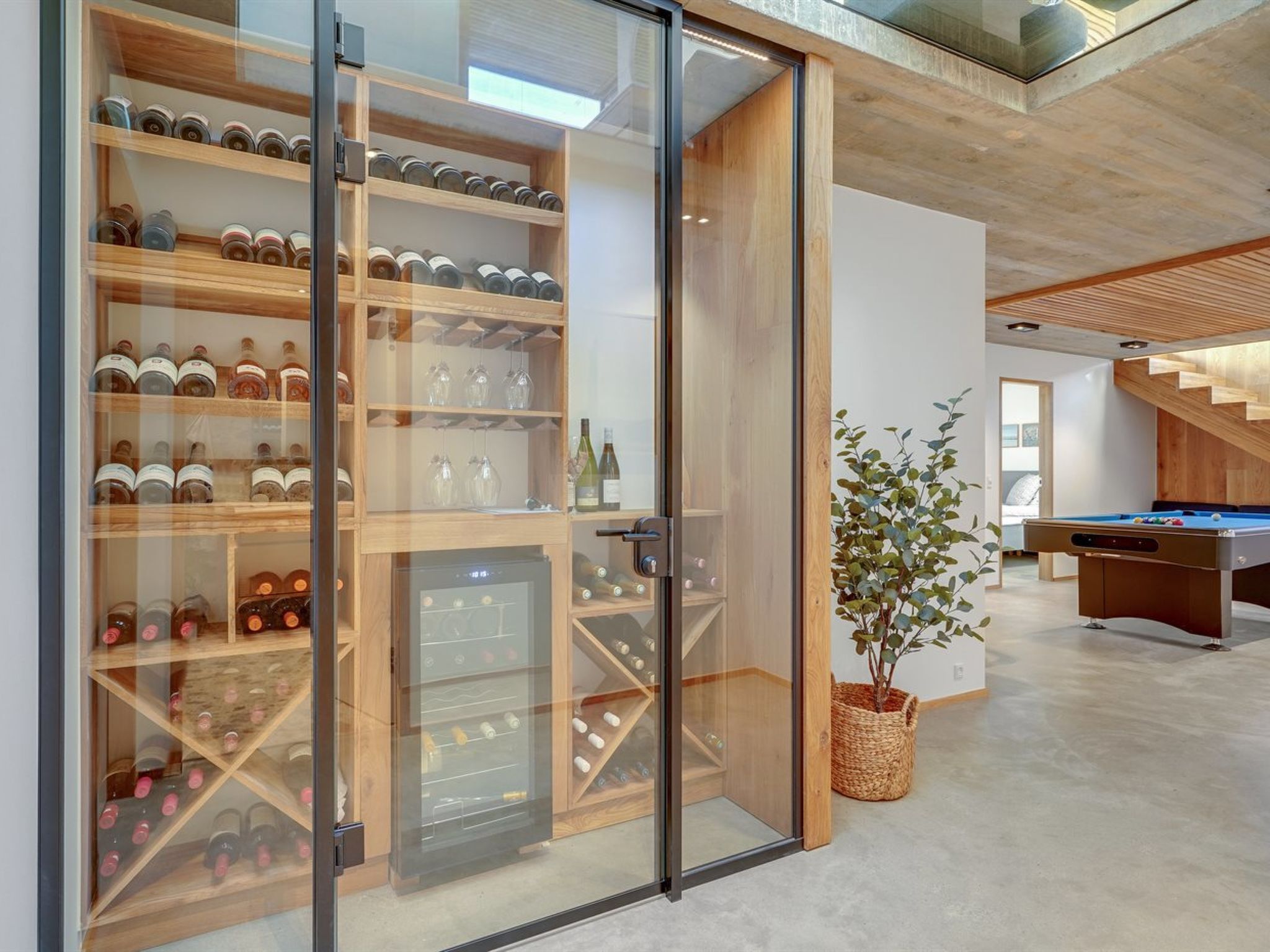 A modern interior with a wine cellar, a pool table, and a staircase.
