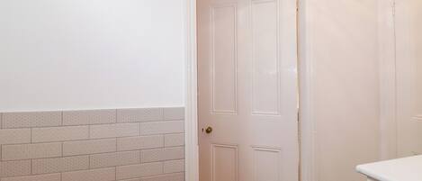 Un couloir avec une porte blanche, un interrupteur et un luminaire fixé au mur.