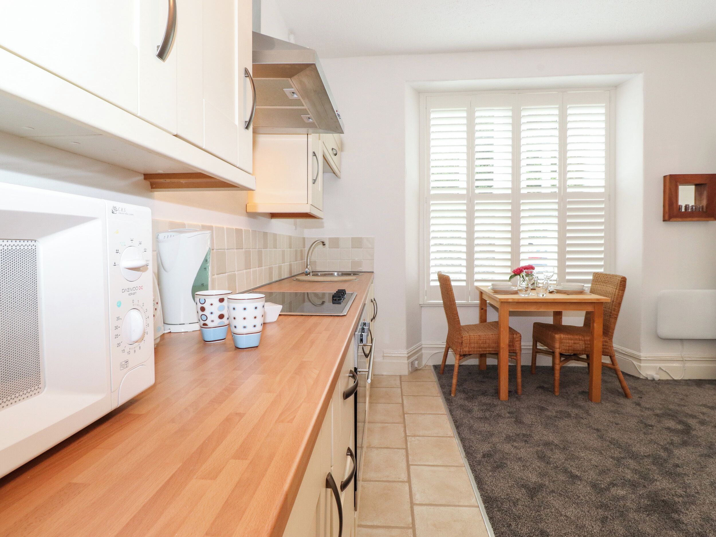 A modern kitchen with white cabinets, a wooden countertop, a built-in microwave, and a dining area with a table and chairs.