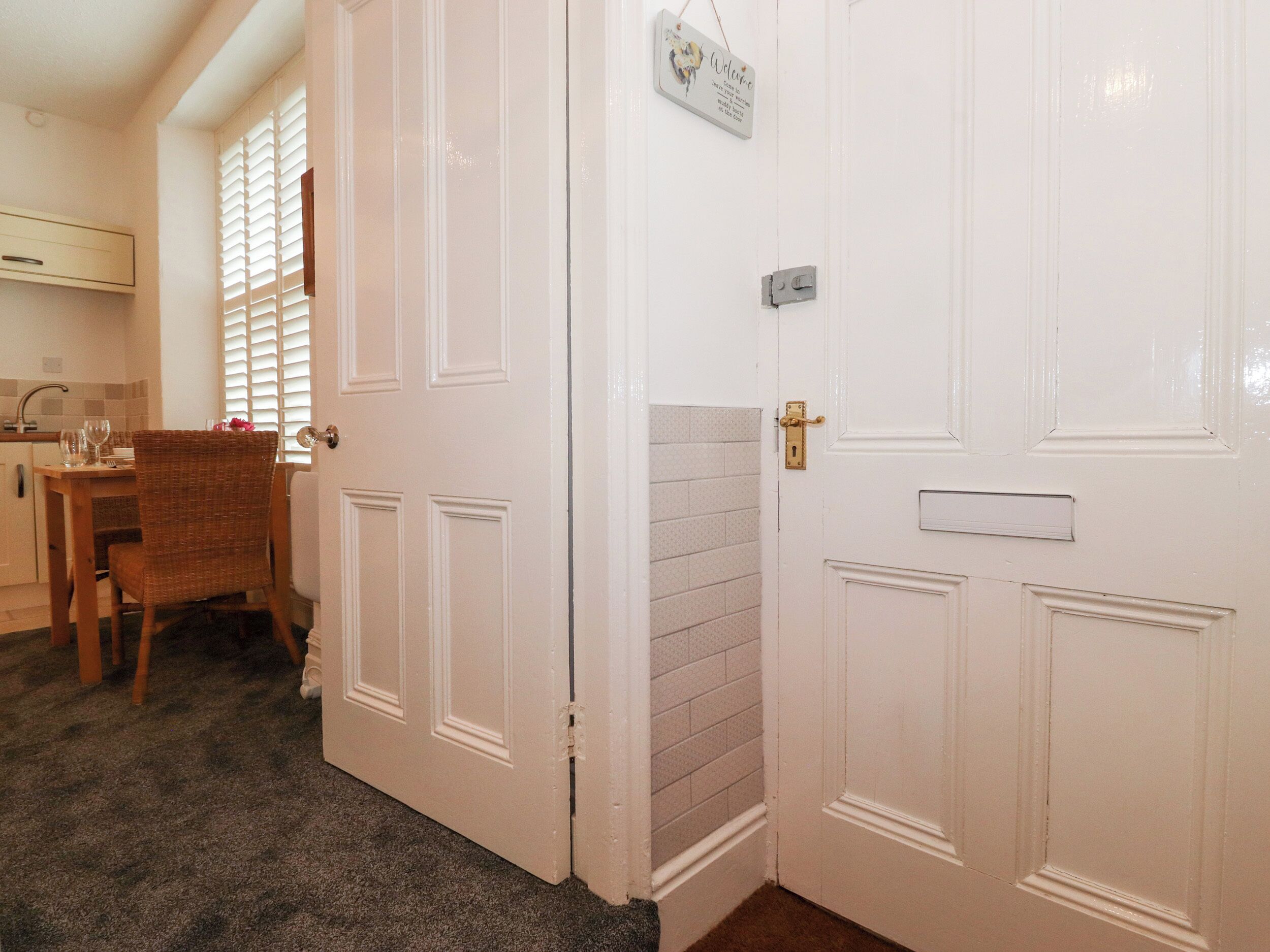 Una habitación con una puerta blanca, una mesita con una silla y una ventana con persianas.