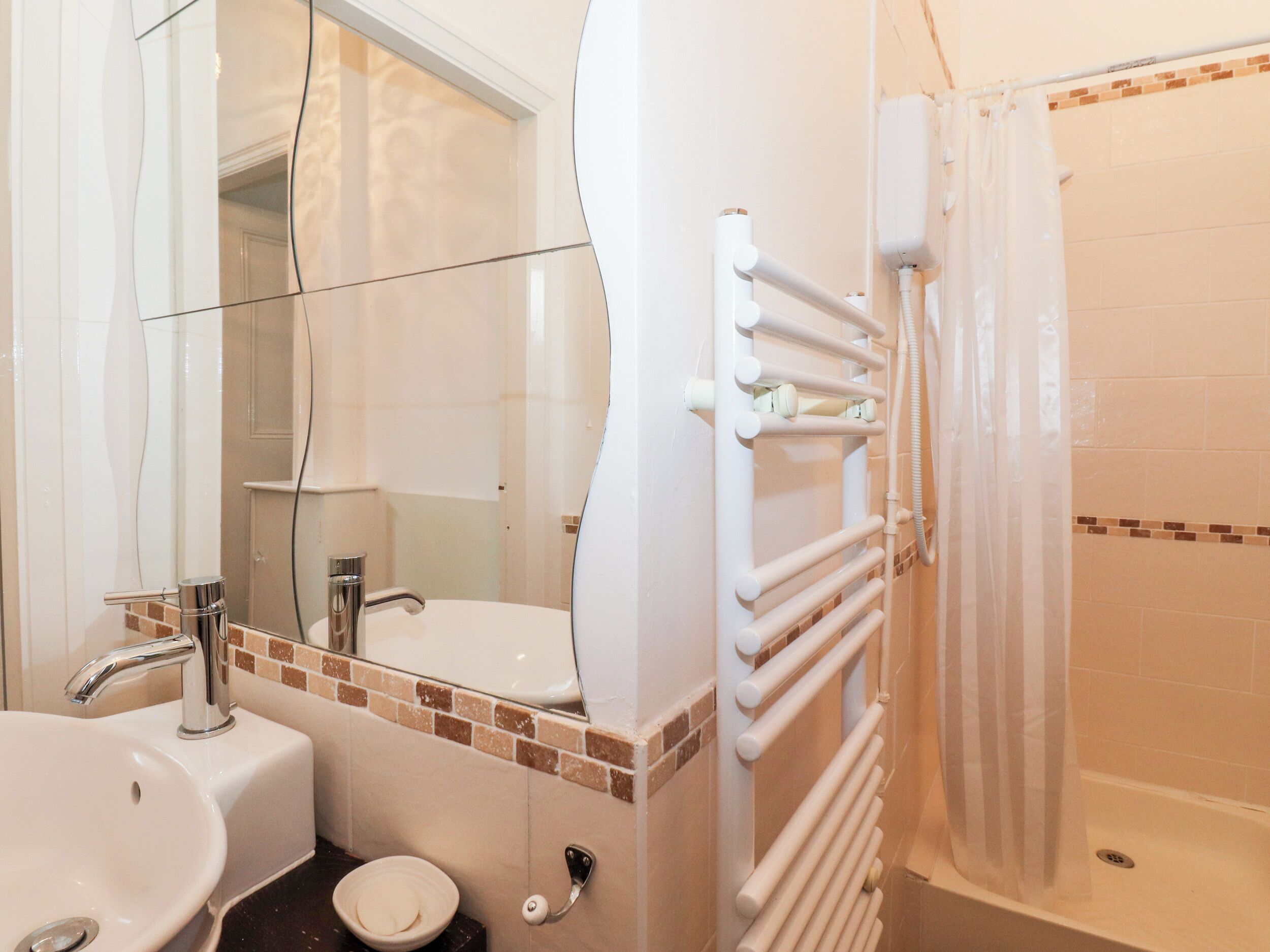 A bathroom with a sink, mirror, and a shower with a towel rack.
