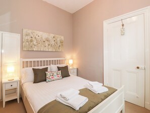A neatly made bed with white linens and a brown throw, flanked by white nightstands with lamps. A floral pillow adds a pop of color. - 1a Biskey Howe (Windermere)