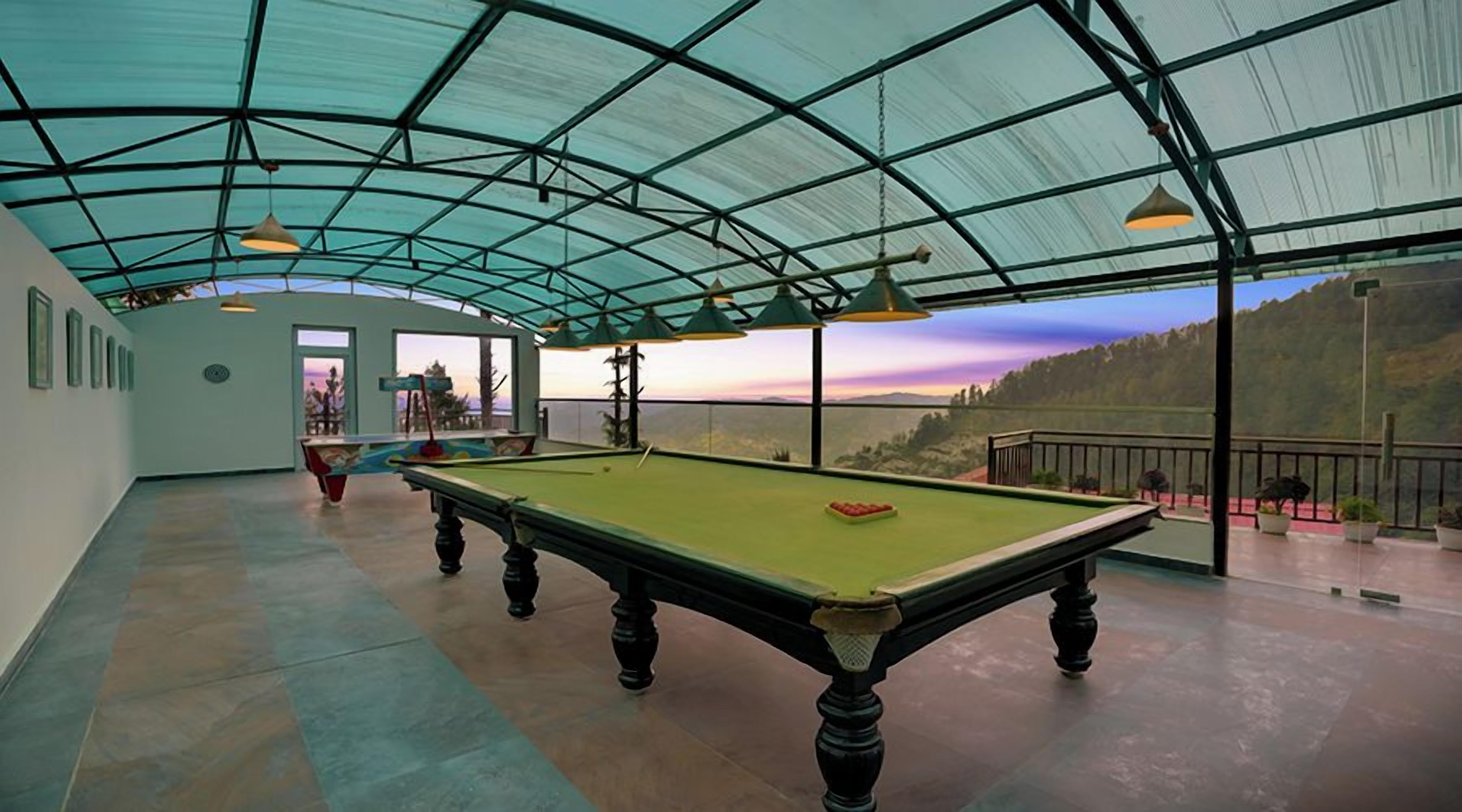 Une table de billard installée dans un espace abrité, avec vue sur un paysage boisé.