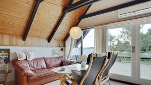 A cozy living room with a wooden ceiling, a leather sofa, a round table, and a dining area with chairs.