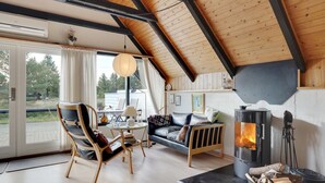 A cozy living room with a fireplace, wooden furniture, and a large window overlooking a scenic outdoor area.