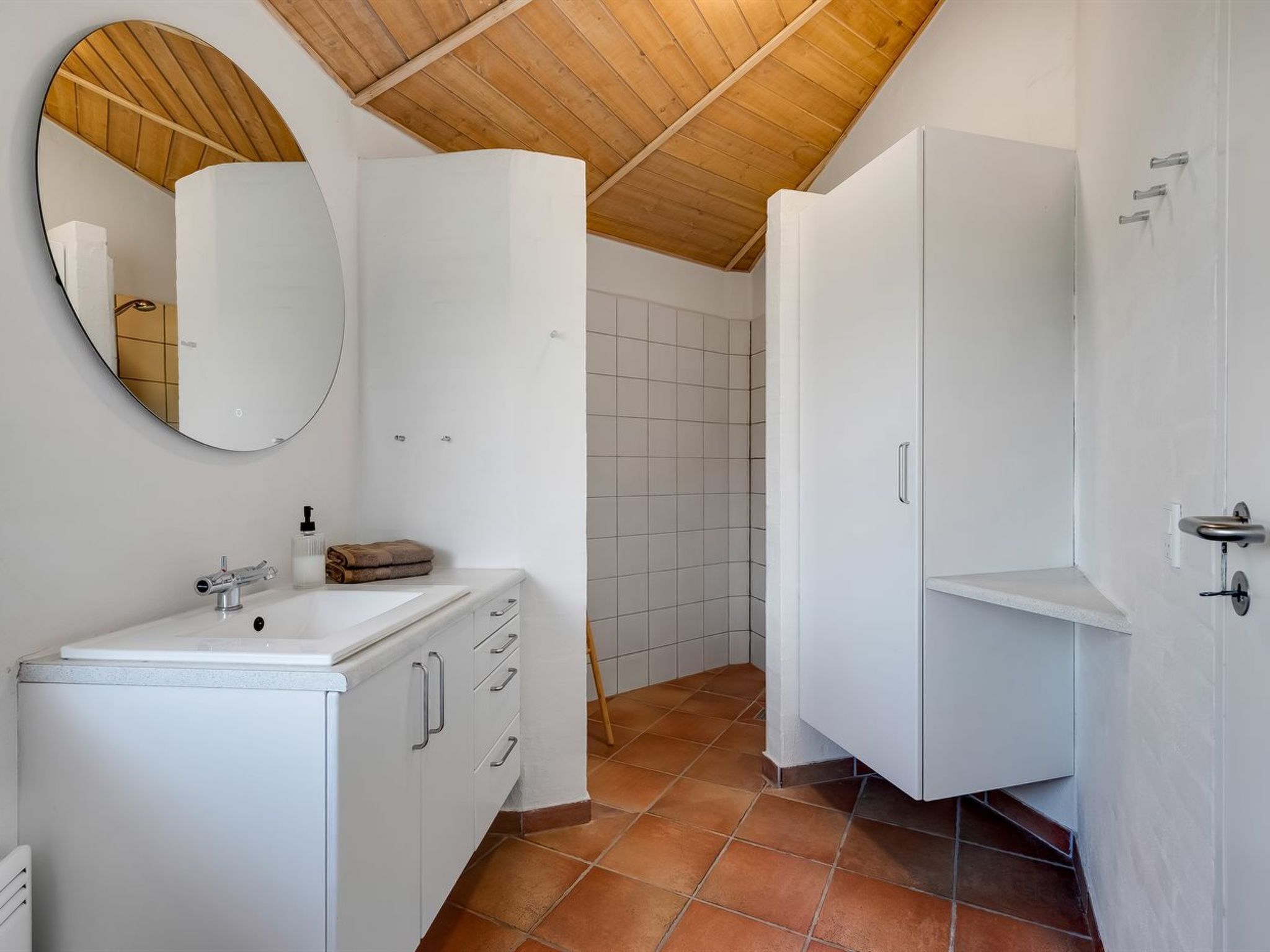 A bathroom with a white sink, mirror, and cabinets, a shower area, and a wooden ceiling.