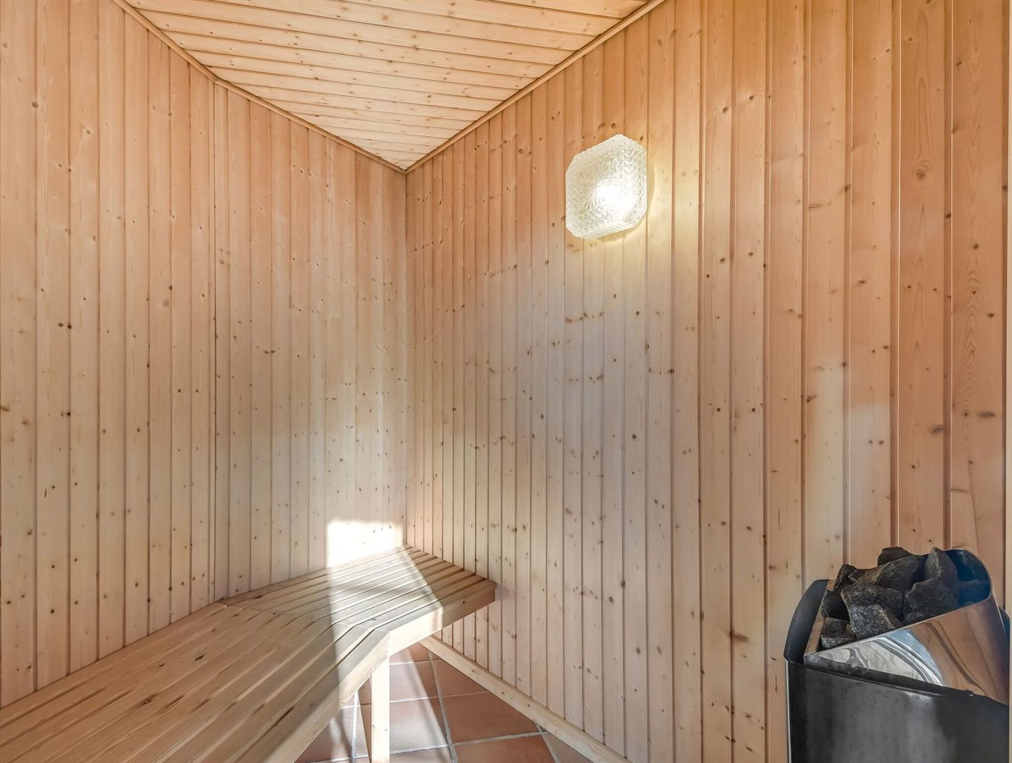 Un sauna avec des murs en bois, un banc et un luminaire.